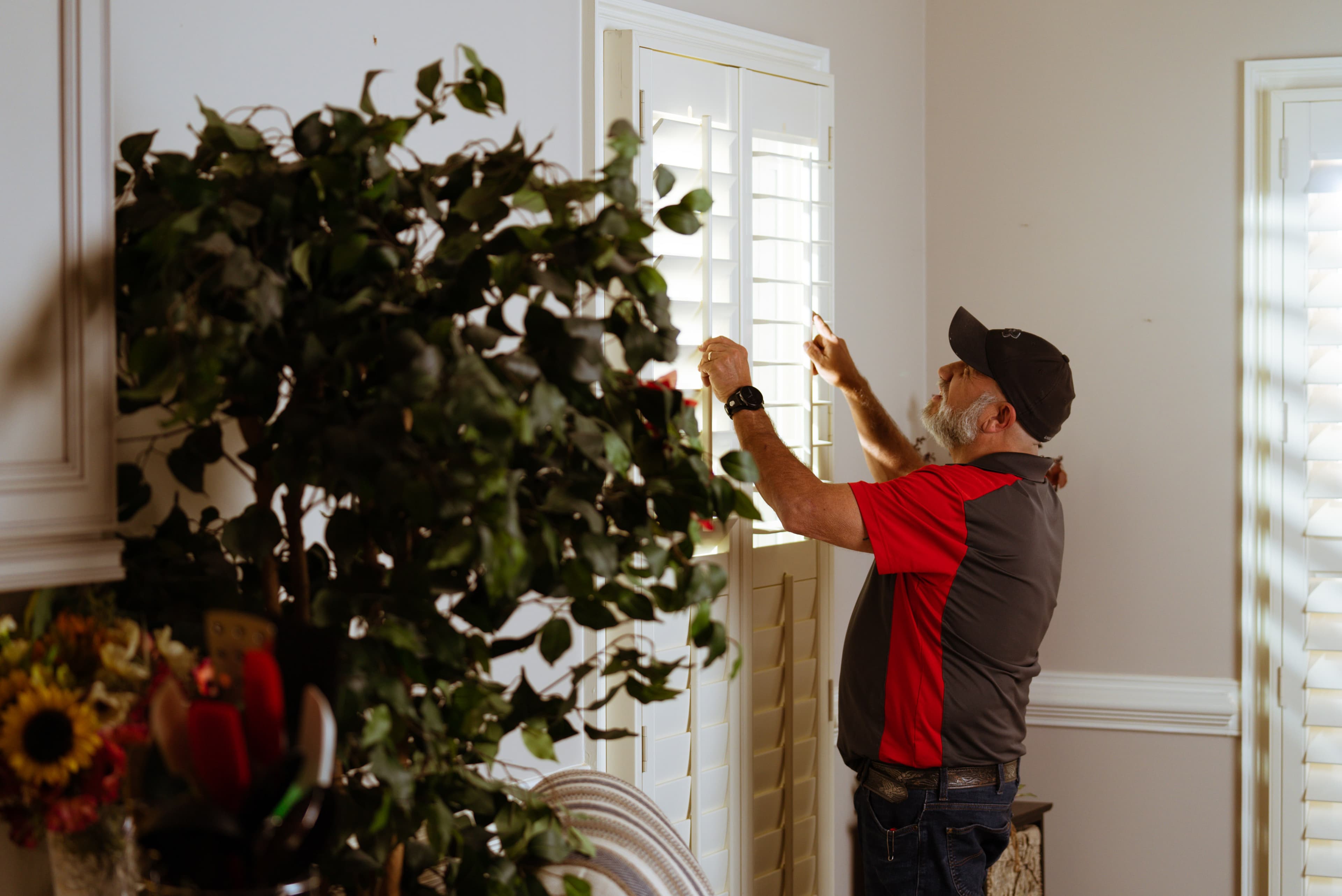 A Blind Guyz installer in a branded polo adjusting newly fitted plantation shutters in a customer's front room.