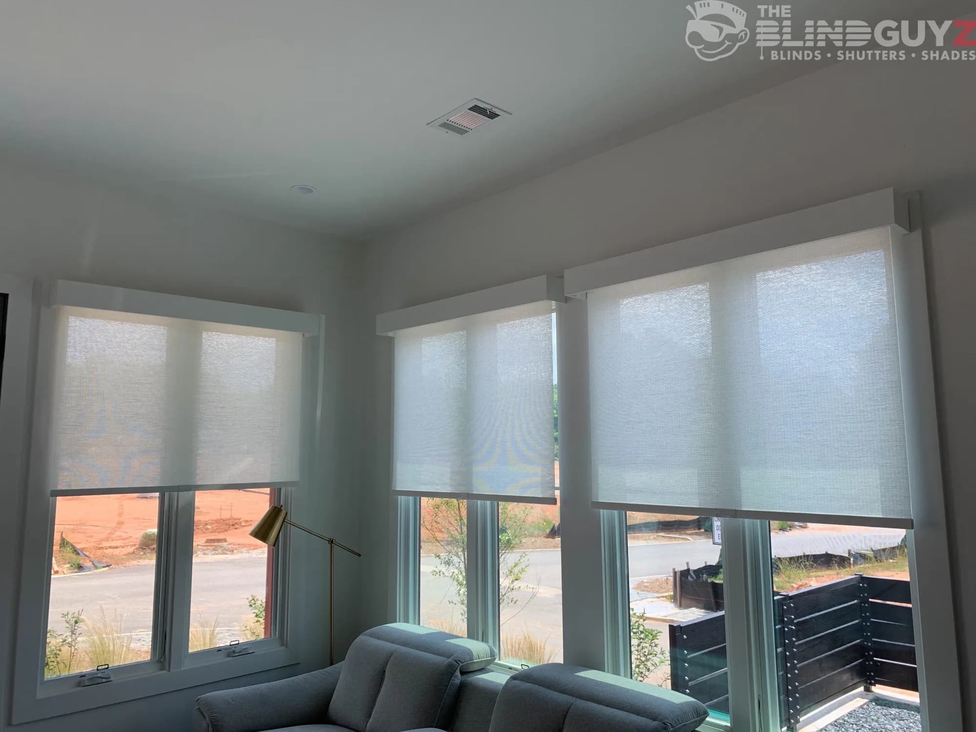 Roller shades under white box valances, half lowered on the corner windows of a living room.