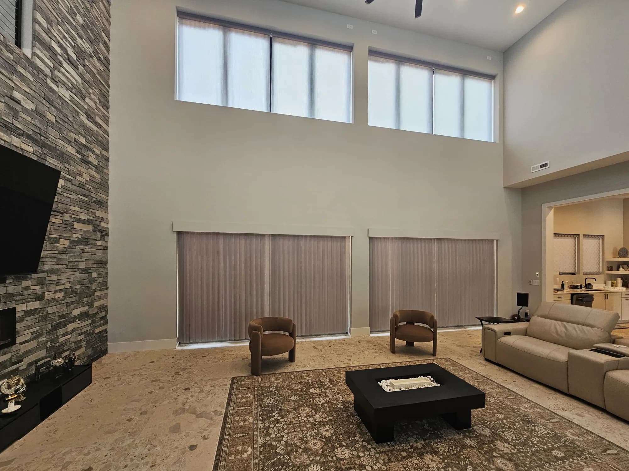 Shades lowered on the high clerestory windows of a two-story great room, with vertical blinds closed across the patio doors below.