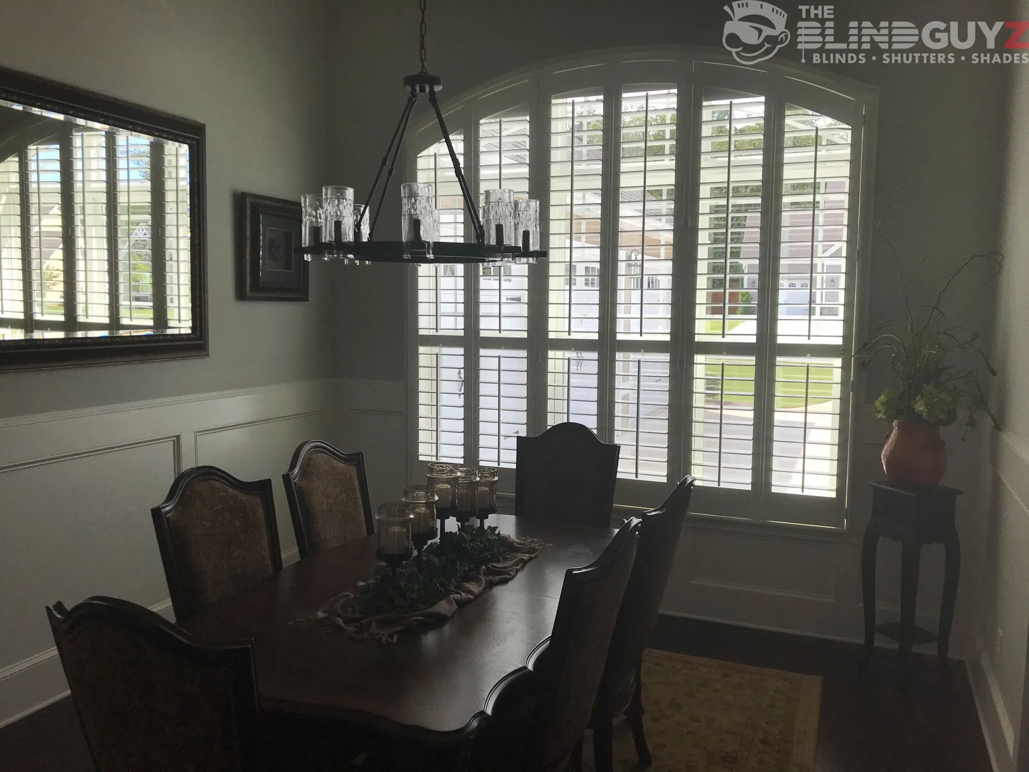 White plantation shutters following the arched top of a dining room window.