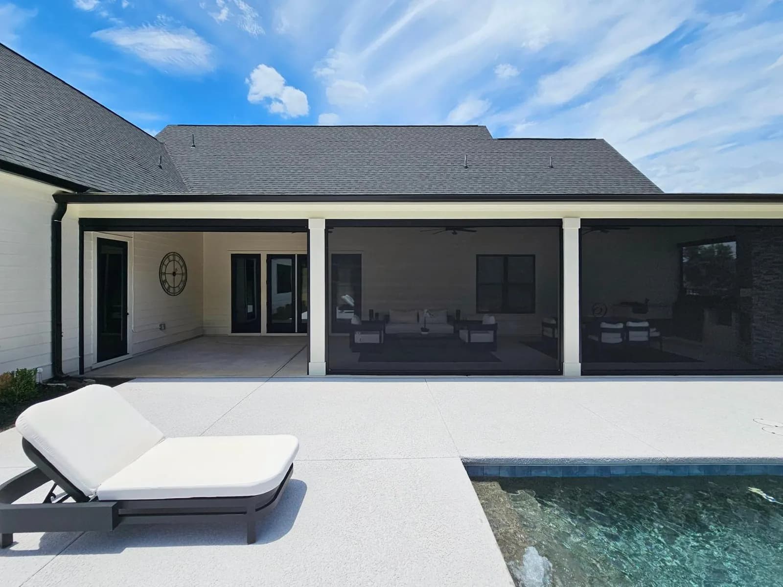 Dark retractable screens lowered across two bays of a covered patio beside a pool, with the third bay left open.