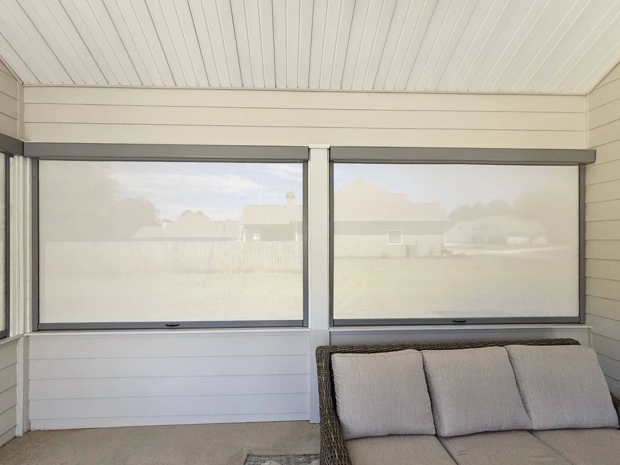 Two retractable screens fully lowered on a covered porch, showing the housing across the top of each opening and the tracks down its sides.