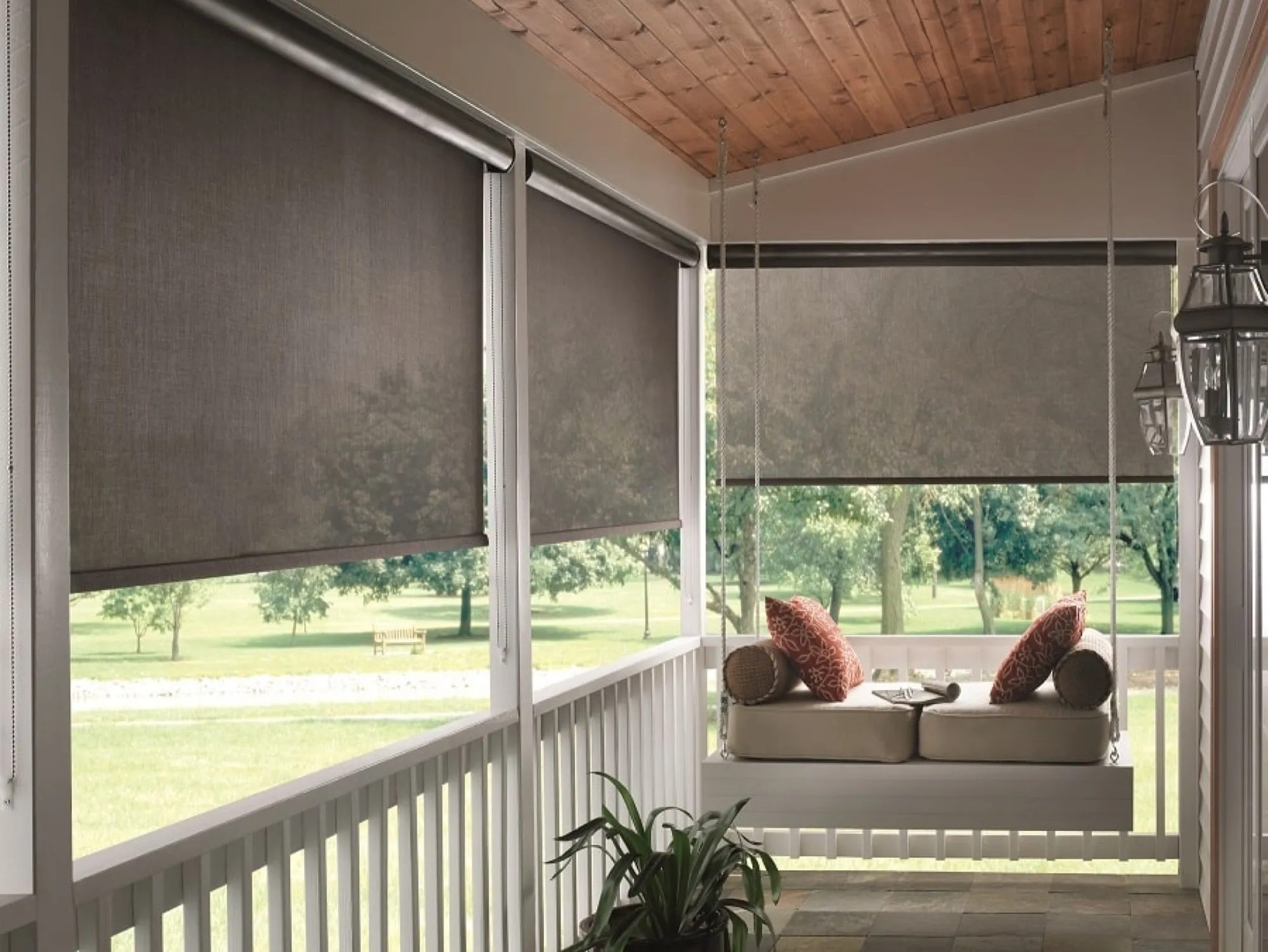 Taupe solar shades lowered partway around a covered porch with a hanging swing bed.