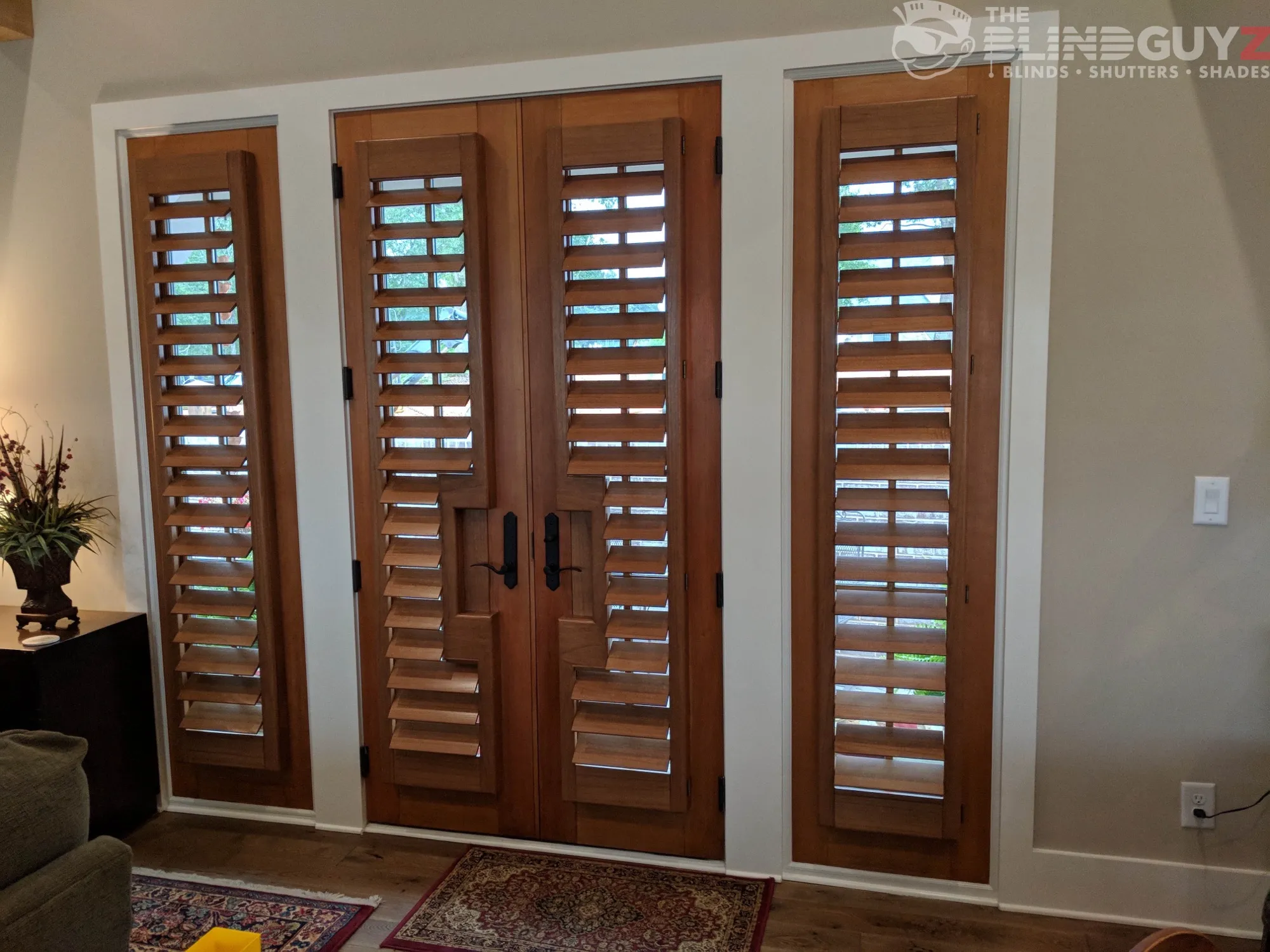 Stained wood plantation shutters on a pair of French doors and both sidelights, cut out around the handles.