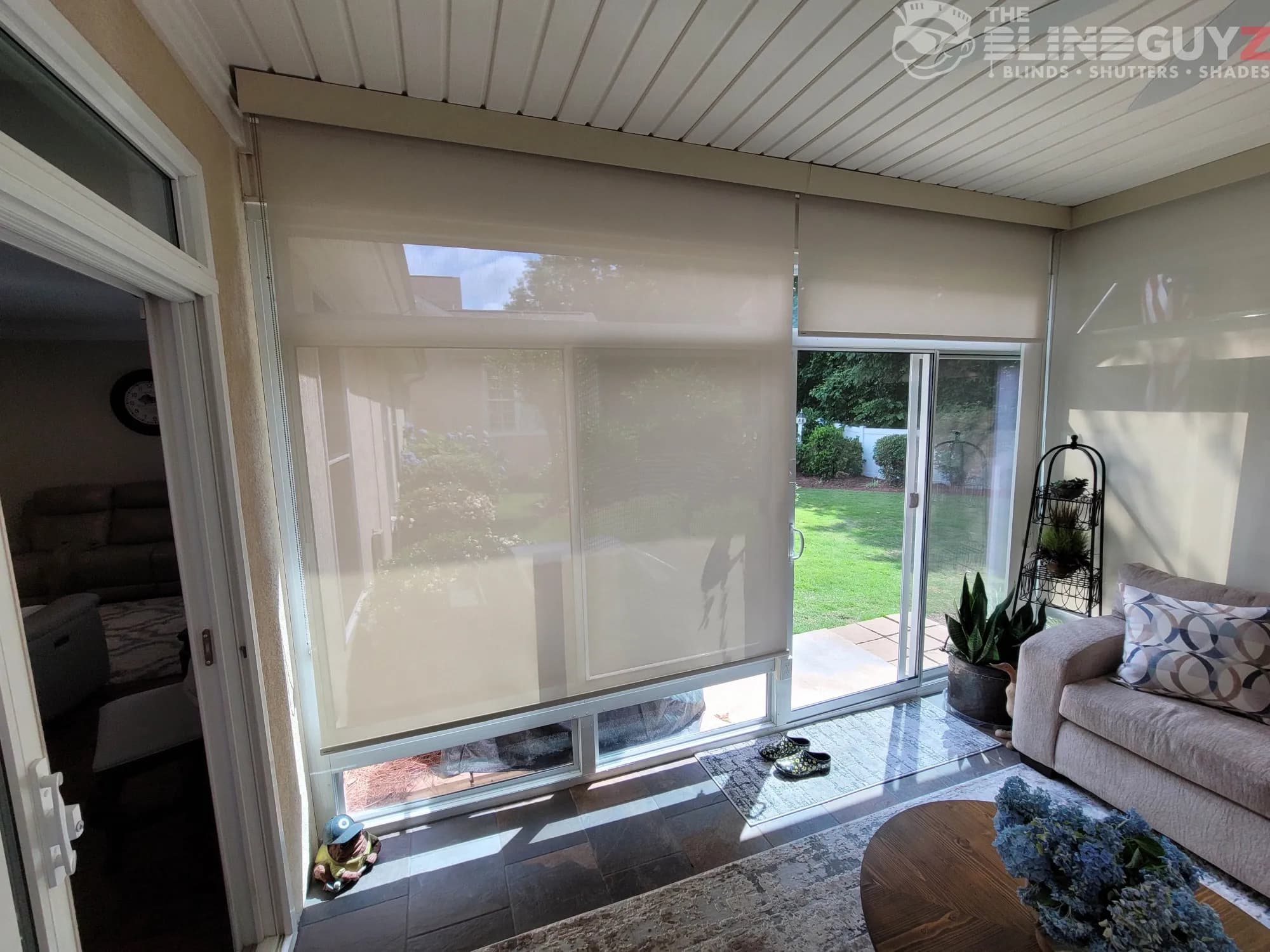 Sand-colored solar roller shades on the tall windows and sliding door of a sunroom.