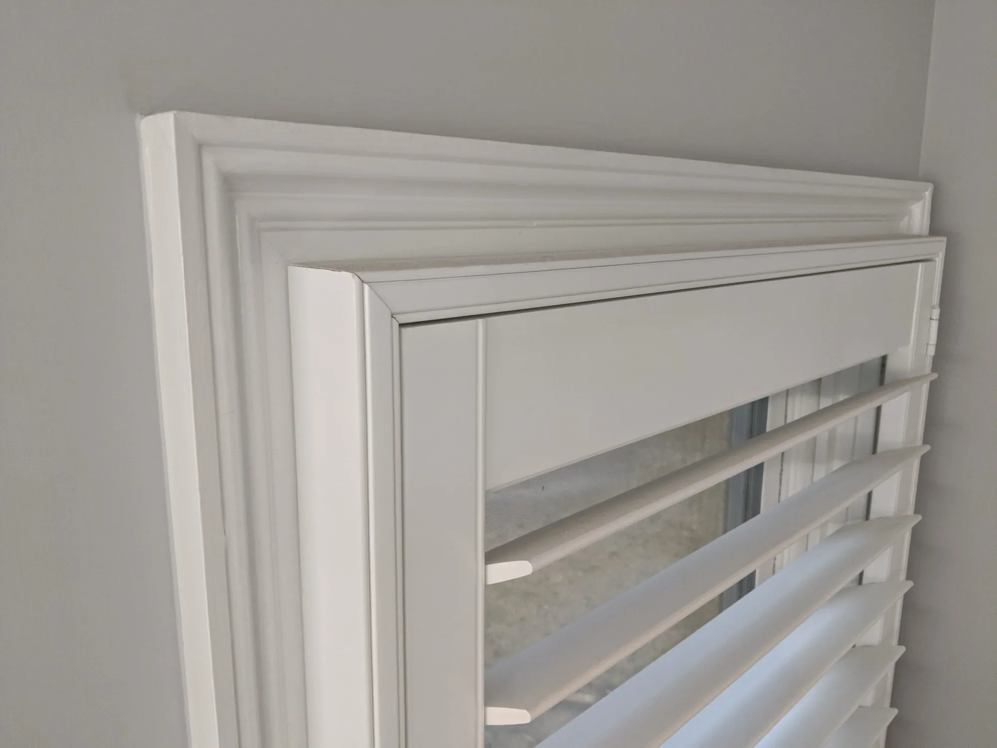 Close-up of a white plantation shutter, showing the decorative frame and the louvers.