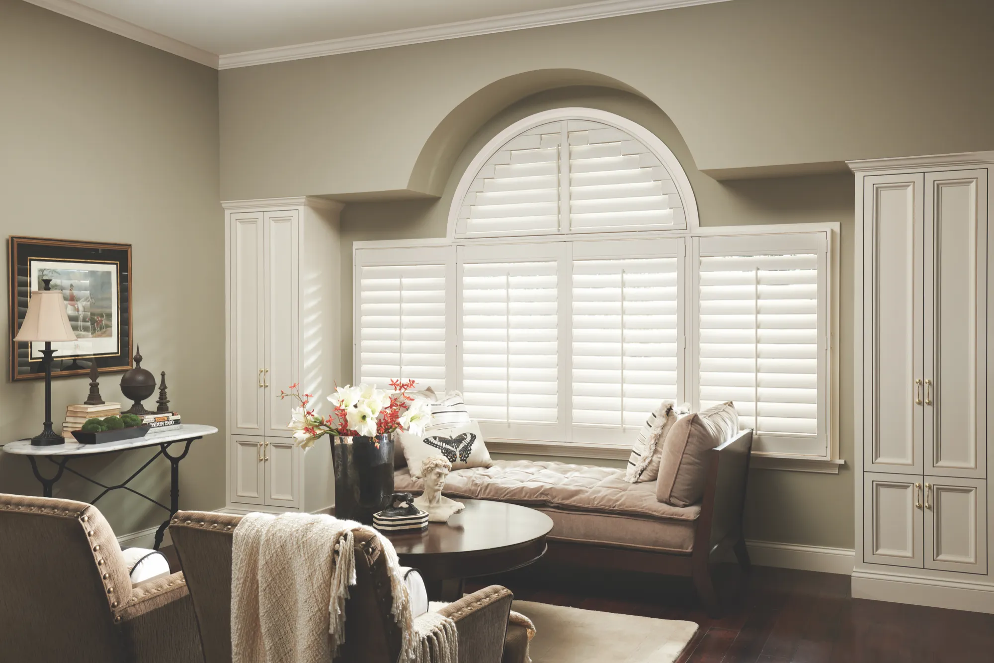 A den bay fitted with white shutters, including a curved panel following the arch of the window above the seat.