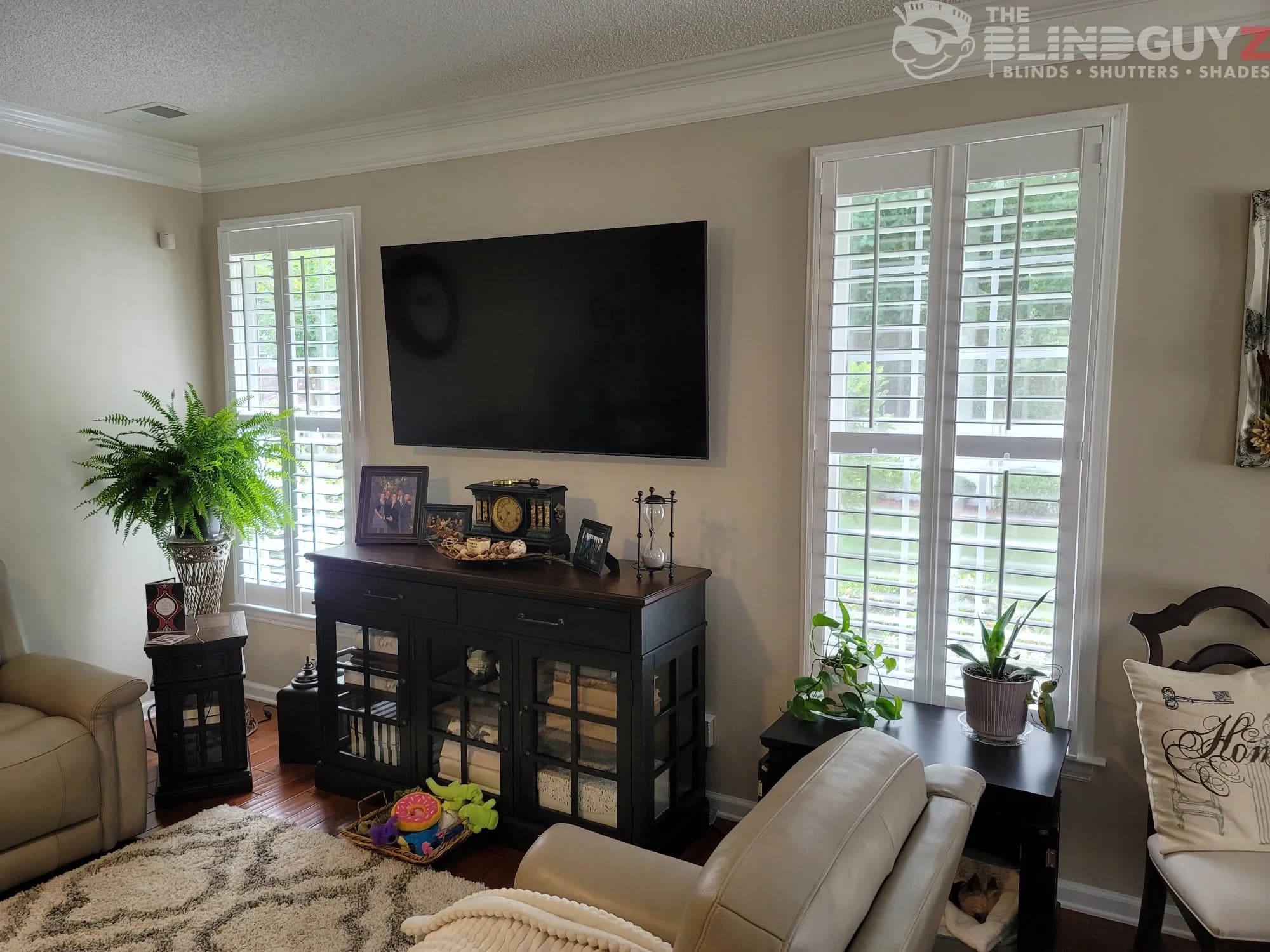 White plantation shutters on two family room windows, either side of a wall-mounted TV.