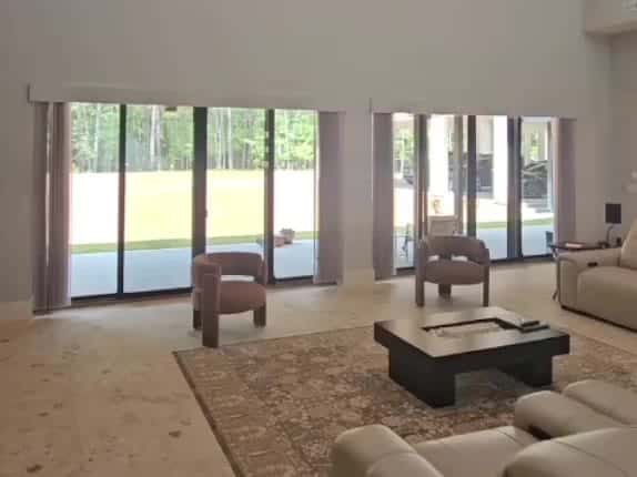 A living room with two sliding patio doors. Motorized vertical blinds close across both doors together, then open again.